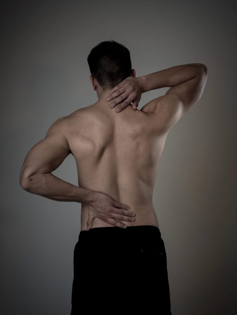 A shirtless man holding his neck and lower back in pain.